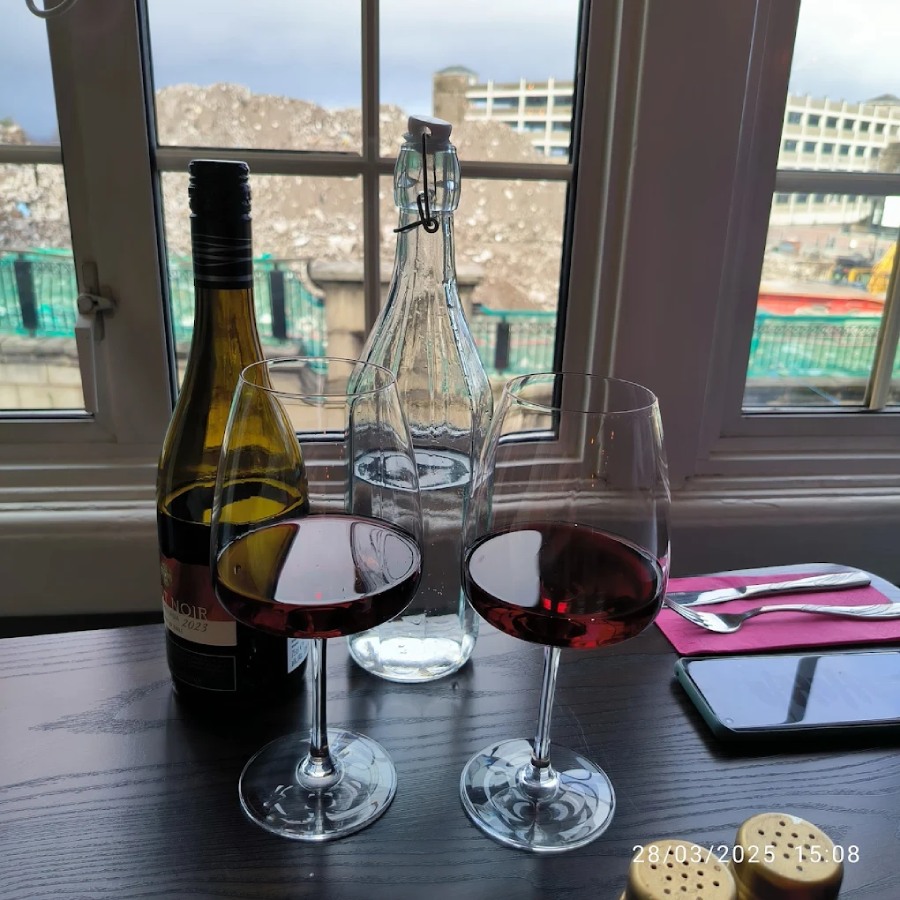   Still life photo of two glasses of red wine, a wine bottle, and a water carafe by 
a window at Greek Theory Falkirk 